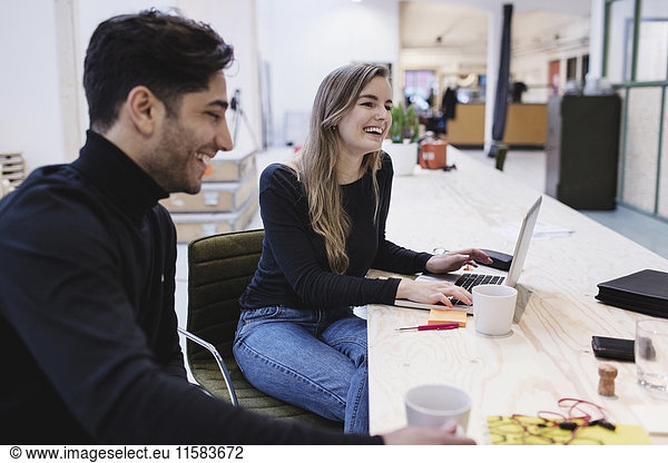 Cheerful woman and man sitting at desk in office