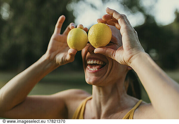 Cheerful woman covering face with lemons