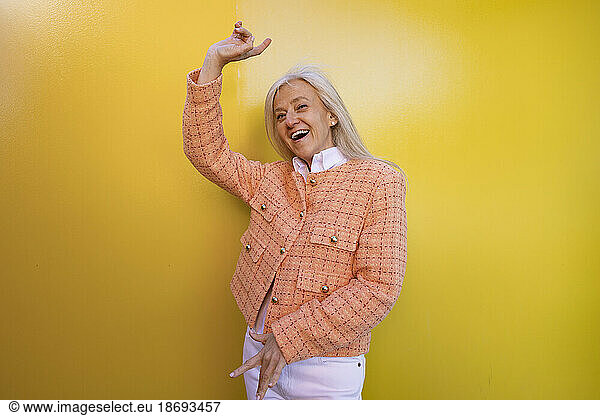Cheerful woman dancing in front of yellow wall