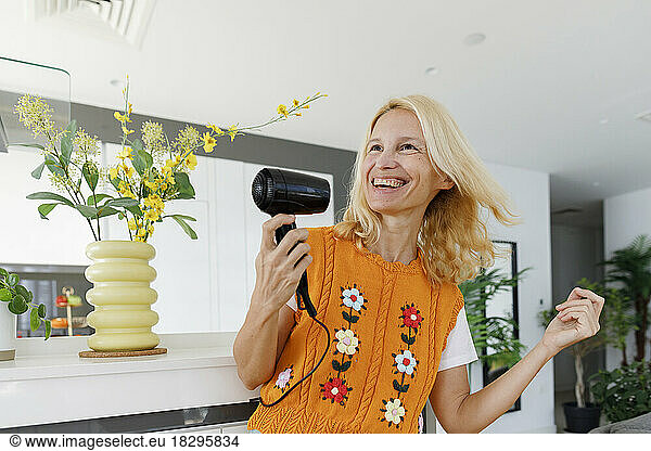 Cheerful woman dancing with hairdryer at home