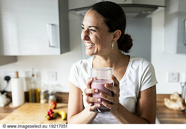 Cheerful woman holding glass of milkshake at home