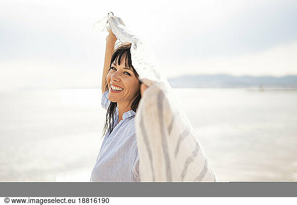 Cheerful woman holding scarf at beach