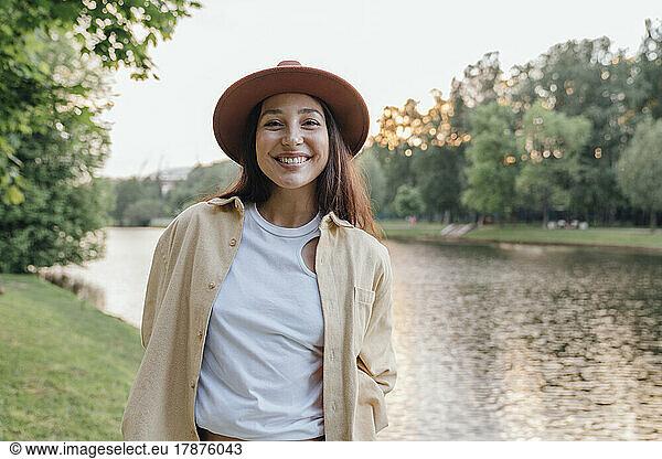 Cheerful woman in hat by lake in park