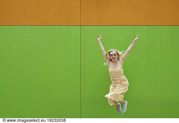 Cheerful woman jumping in front of green wall