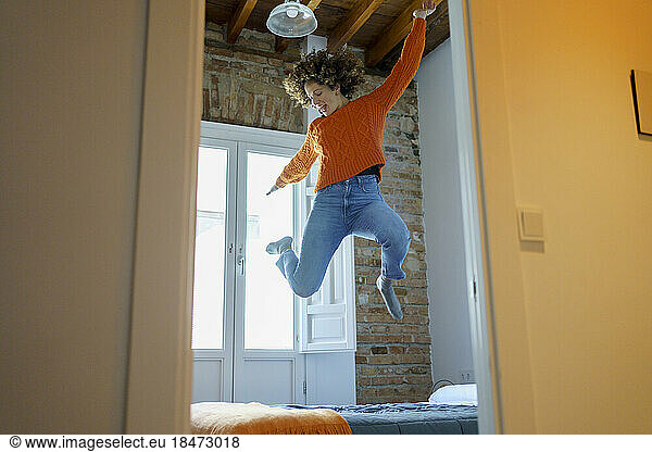 Cheerful woman jumping on bed at home