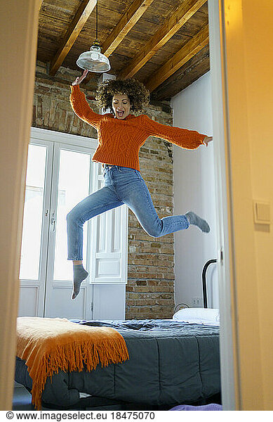 Cheerful woman jumping on bed in bedroom at home