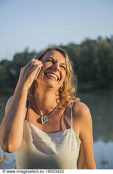 Cheerful woman laughing while talking on smart phone at riverbank  Bavaria  Germany