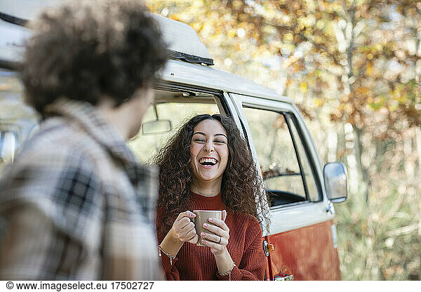 Cheerful woman laughing with man in foreground at autumn forest