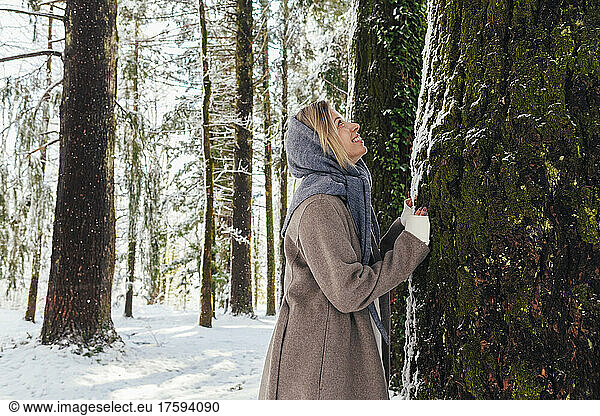 Cheerful woman leaning on tree trunk in forest