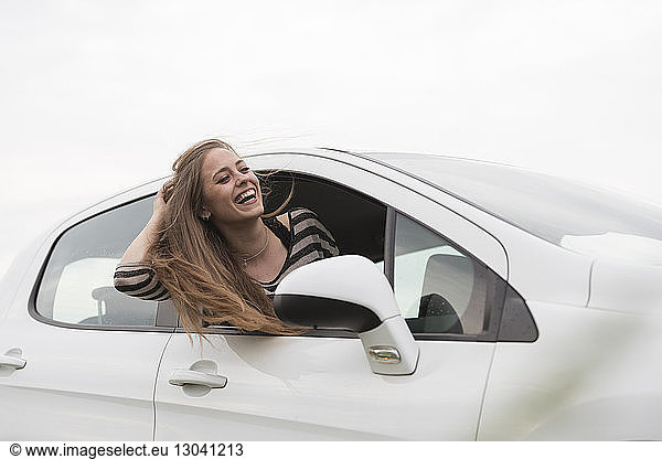 Cheerful woman peeking out from car window against clear sky