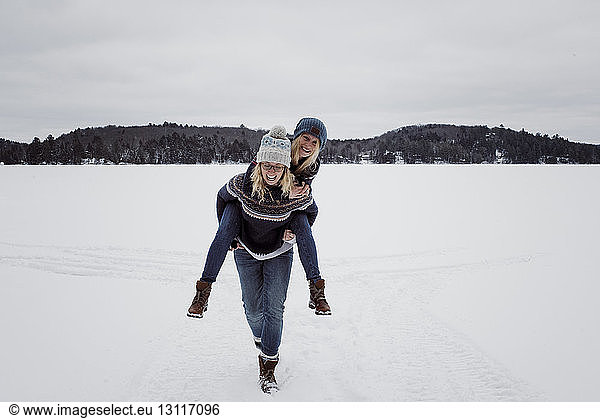 Cheerful woman piggybacking friend on snow during winter