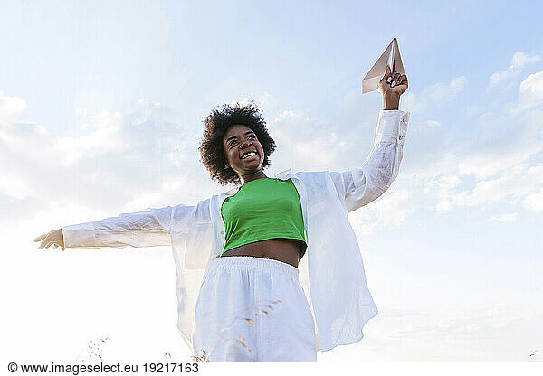 Cheerful woman playing with paper plane in field