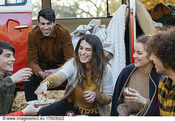 Cheerful woman serving cake to friends outside van on picnic