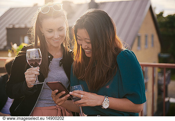 Cheerful woman showing her mobile phone to female friend on terrace during sunset