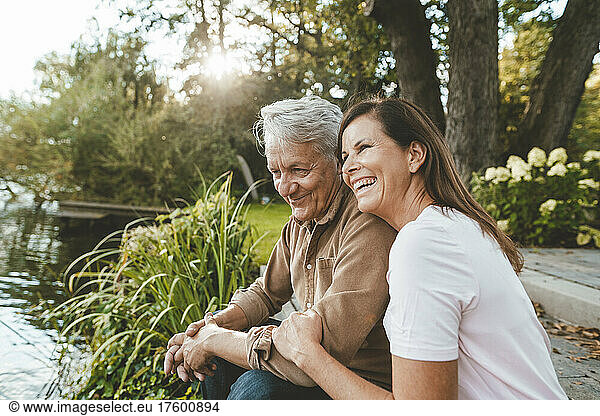 Cheerful woman sitting with senior man by lake
