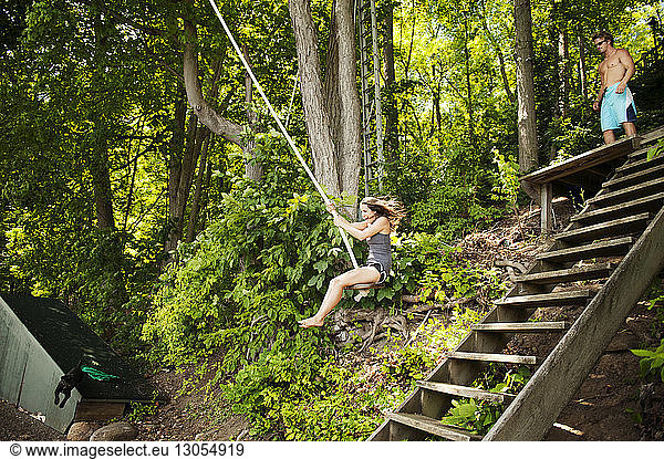 Cheerful woman swinging on rope in forest