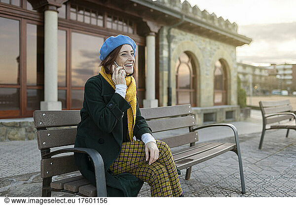 Cheerful woman talking on smart phone sitting on bench