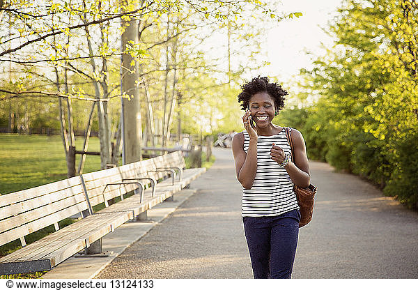 Cheerful woman using smart phone while walking on footpath in park