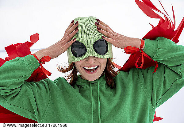 Cheerful woman wearing green knit hat with head in hands against sky