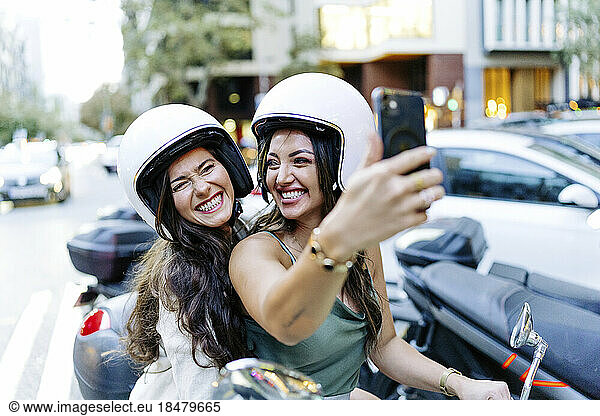Cheerful woman wearing helmet taking selfie through smart phone