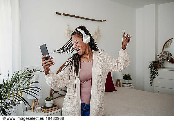 Cheerful woman wearing wireless headphones dancing in bedroom at home