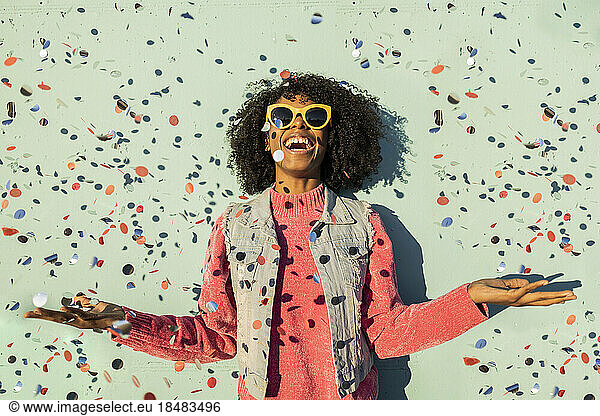 Cheerful woman with confetti enjoying in front of green wall