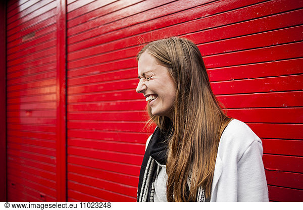 Cheerful woman with eyes closed standing against red shutter