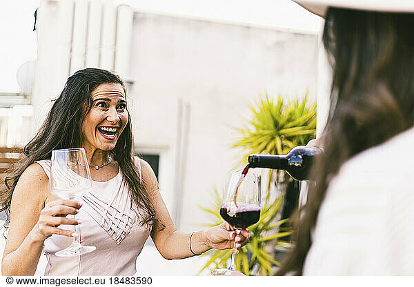 Cheerful woman with friend pouring wine in glass