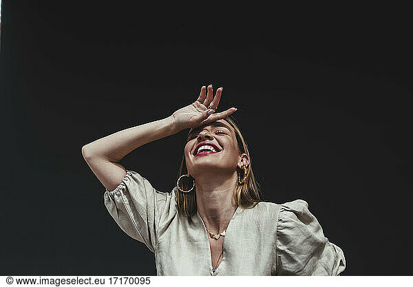 Cheerful woman with hand on head against black background