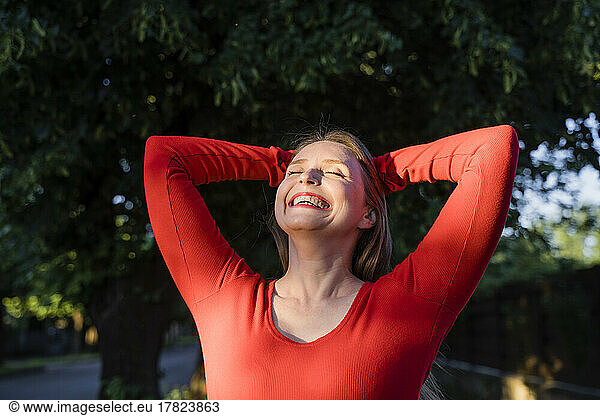 Cheerful woman with hands behind head enjoying sunlight