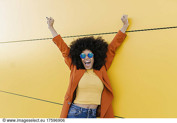 Cheerful woman with hands raised in front of wall