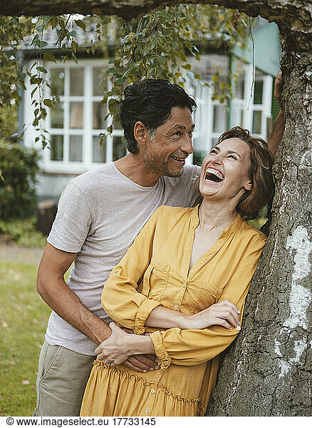 Cheerful woman with man leaning on tree trunk