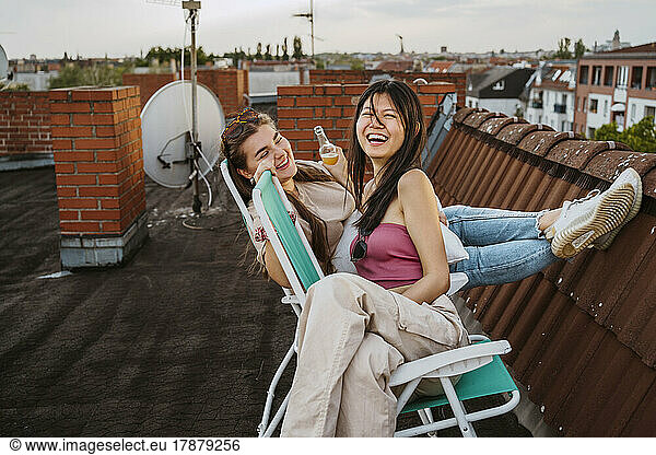 Cheerful women enjoying while sitting on chair at rooftop