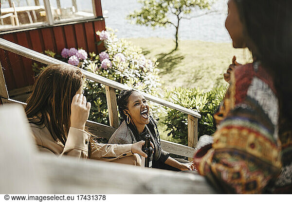 Cheerful women talking while sitting on staircase during party at front yard