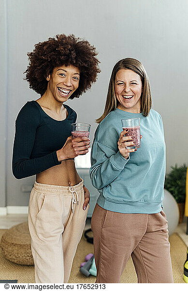 Cheerful women with glasses of smoothie standing together in living room at home
