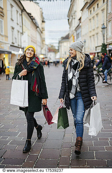 Cheerful women with shopping bags walking on footpath at market