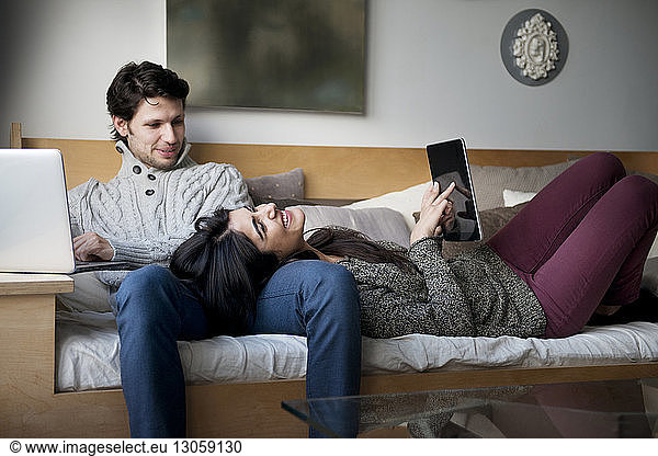 Cheerful young couple using technologies while relaxing on sofa
