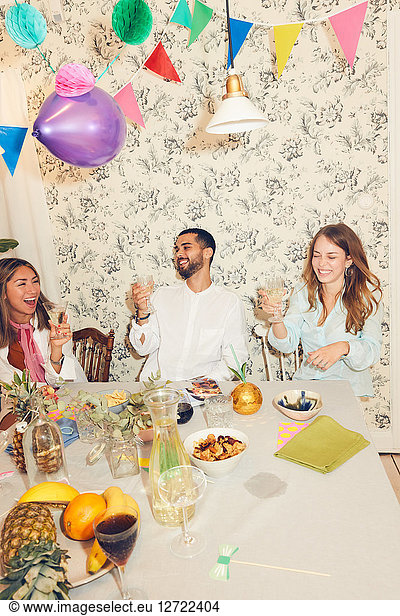 Cheerful young friends celebrating while sitting at dining table during dinner party