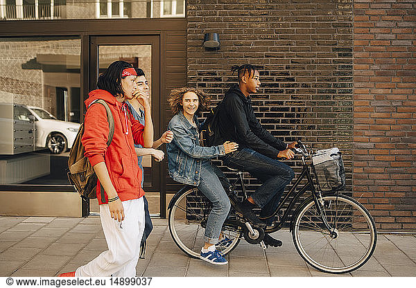 Cheerful young man looking at friends while riding on bicycle in city