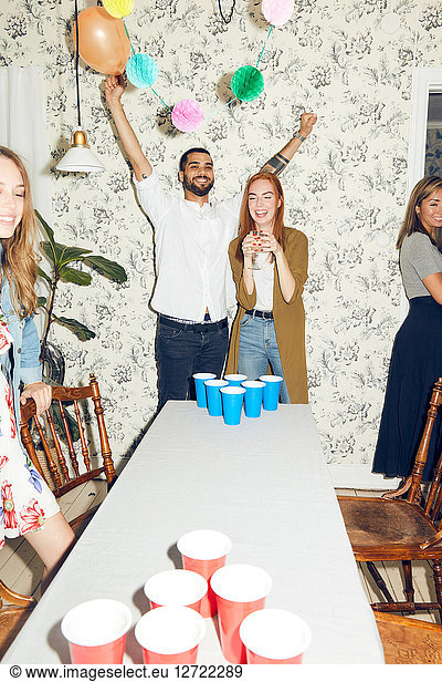 Cheerful young man standing with arms raised by female friend at dinner party