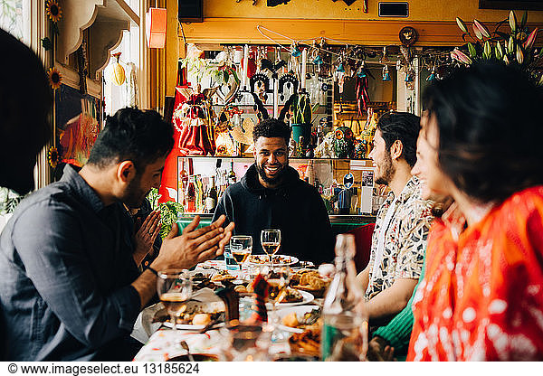 Cheerful young multi-ethnic friends enjoying brunch while sitting at table in restaurant