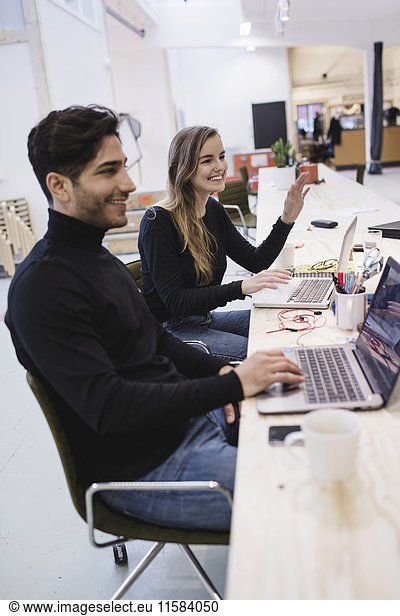 Cheerful young woman and man looking away while sitting at desk in office