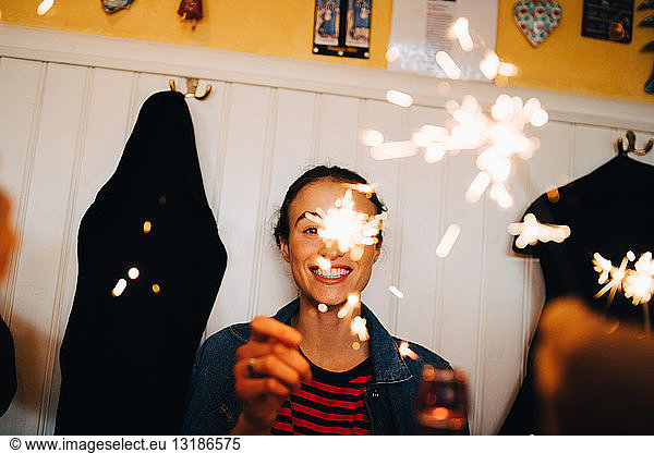 Cheerful young woman holding sparkler while enjoying dinner party at restaurant