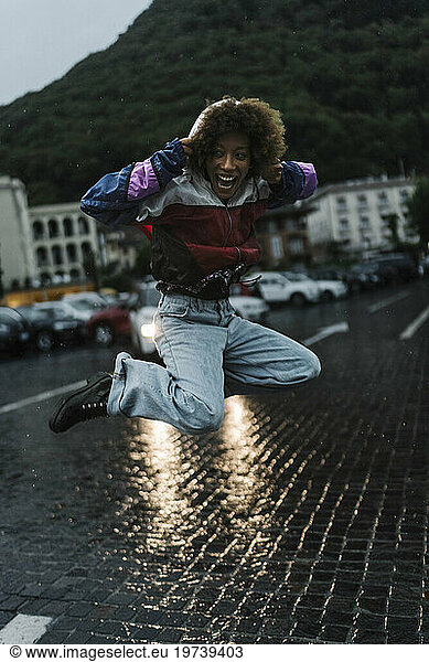 Cheerful young woman jumping in rain