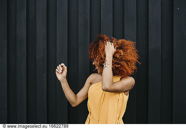 Cheerful young woman shaking hair while standing against wall