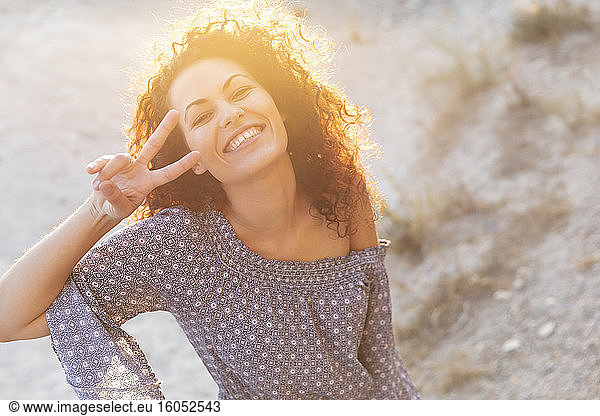 Cheerful young woman showing peace sign during sunny day