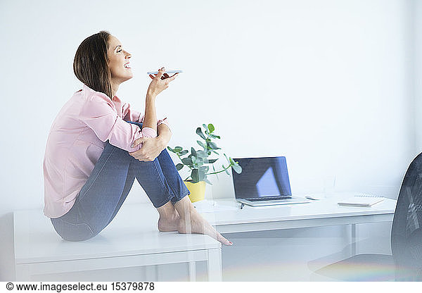 Cheerful young woman sitting on desk and talking on phone