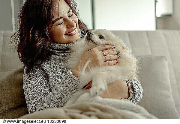 Cheerful young woman stroking Pomeranian dog at home