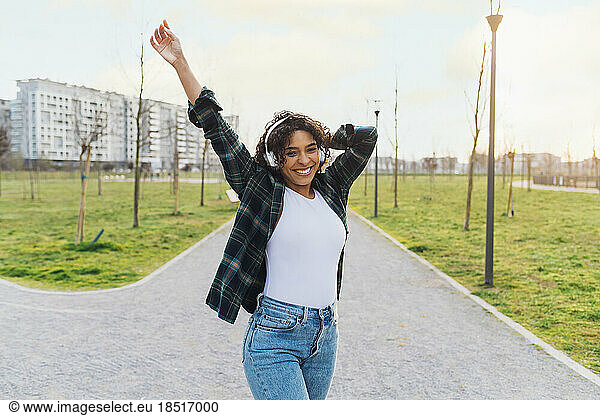Cheerful young woman wearing wireless headphones dancing on footpath