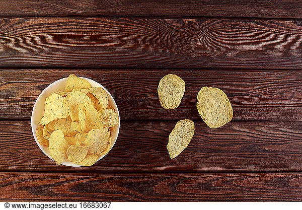 Cheese and chive potato crisp snack in brown bowl on wooden background top view